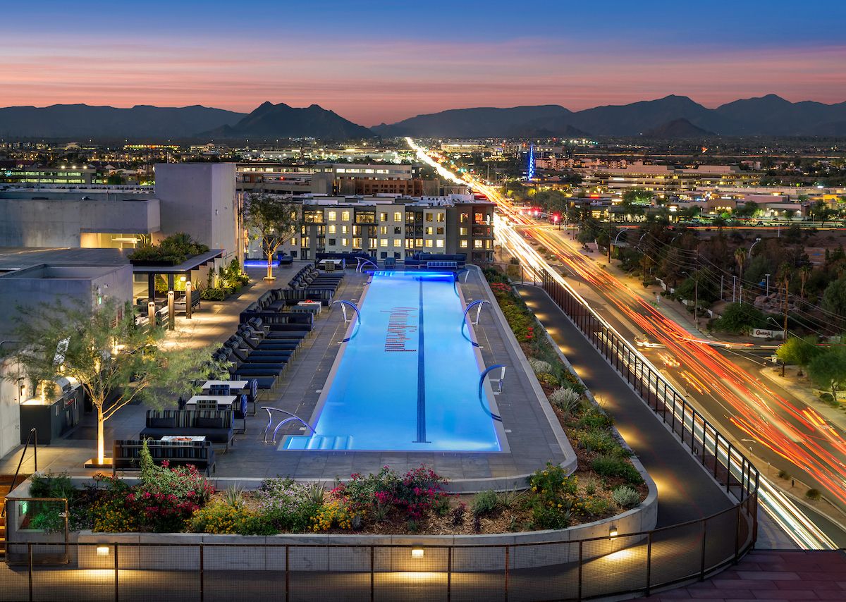 Rooftop pool at 7190-03 Residences lit at dusk, with city lights, lounge chairs, mountains, and Optima Kierland views.