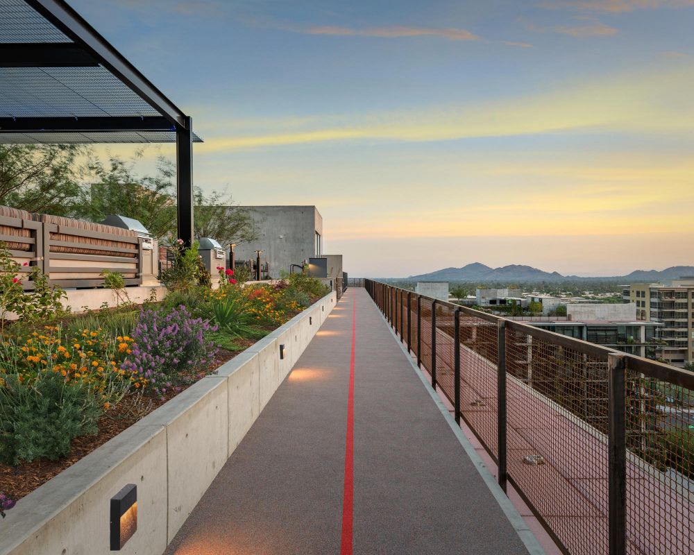 Rooftop garden and walking path at sunset, overlooking city buildings and distant mountains.