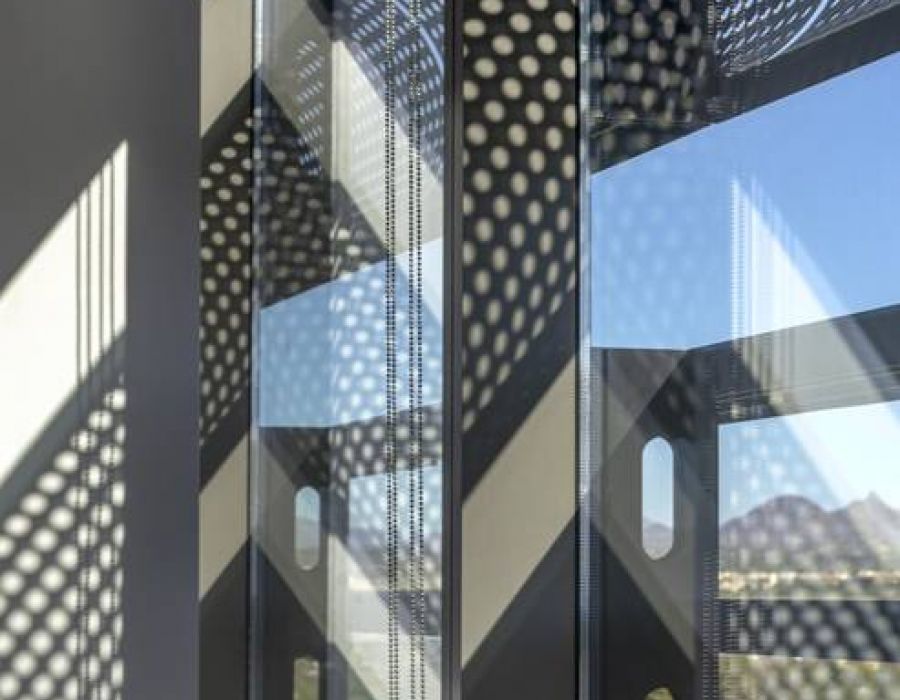 Sunlight casts geometric and dotted shadow patterns on tall glass windows with a mountain view outside.