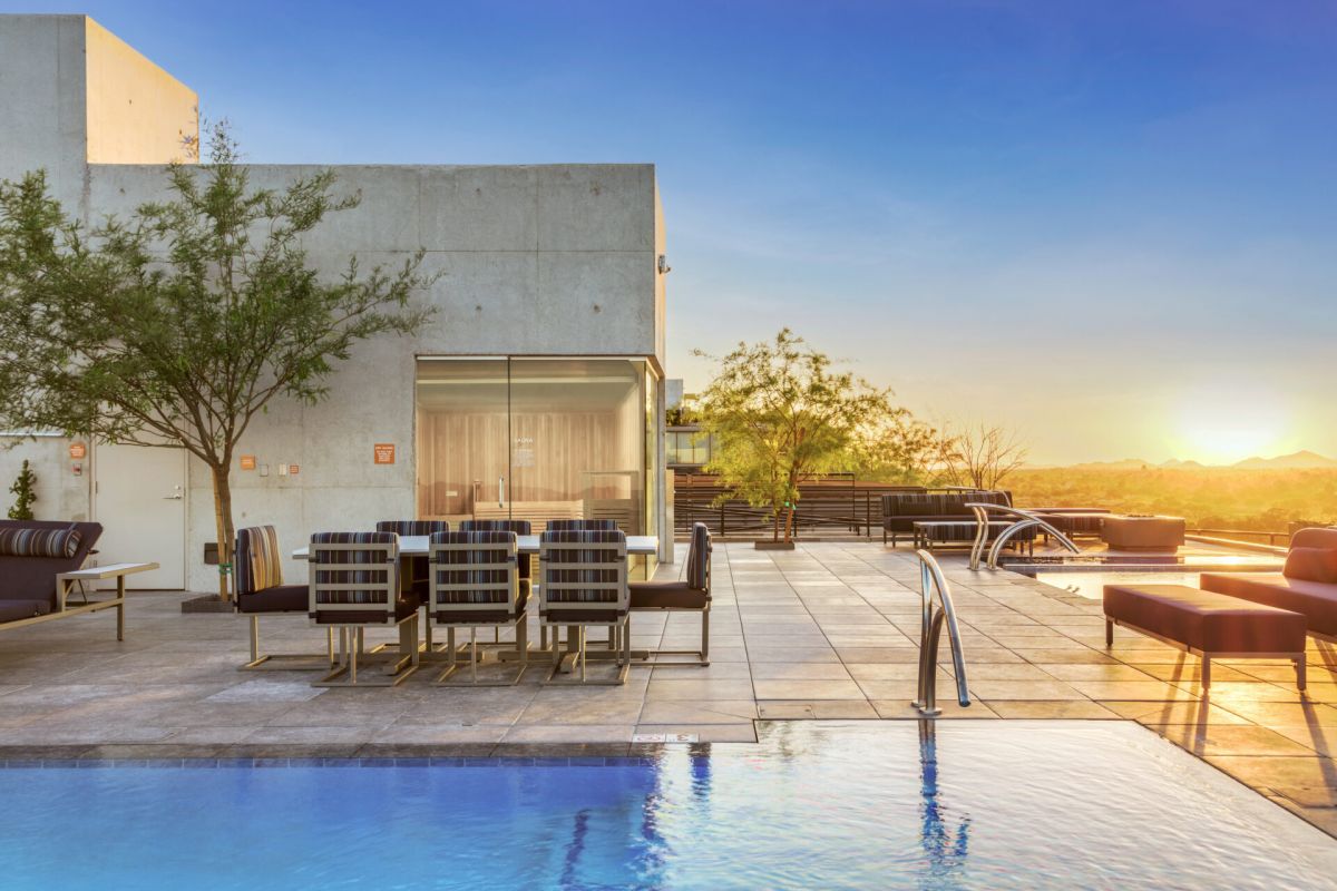 Modern rooftop pool and lounge at sunset, featuring seating, trees, and mountain views—designed with sustainable development in mind.