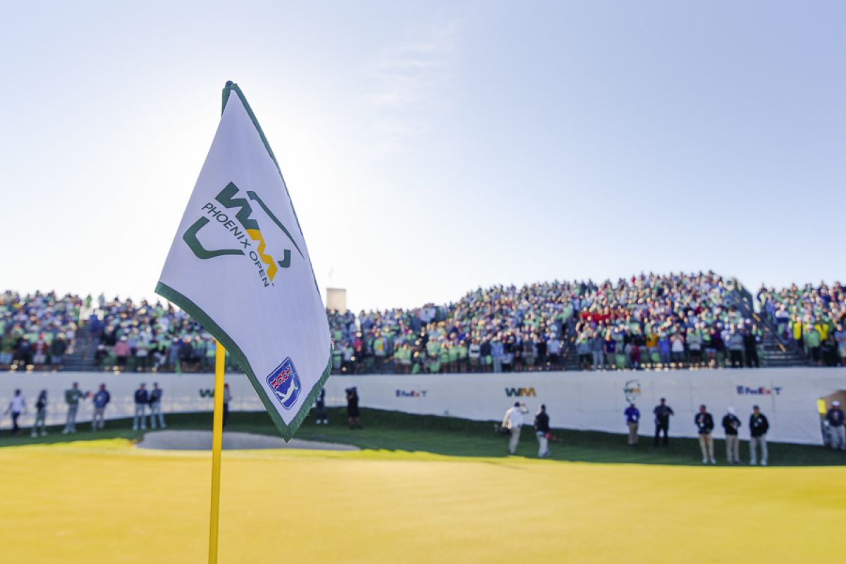 A golf flag with the 2025 WM Phoenix Open logo stands before a large crowd at the Scottsdale golf tournament.