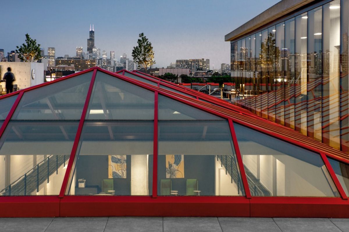 Rooftop view of a modern building with glass ceiling panels, showcasing Optima® Living design against a city skyline at dusk.