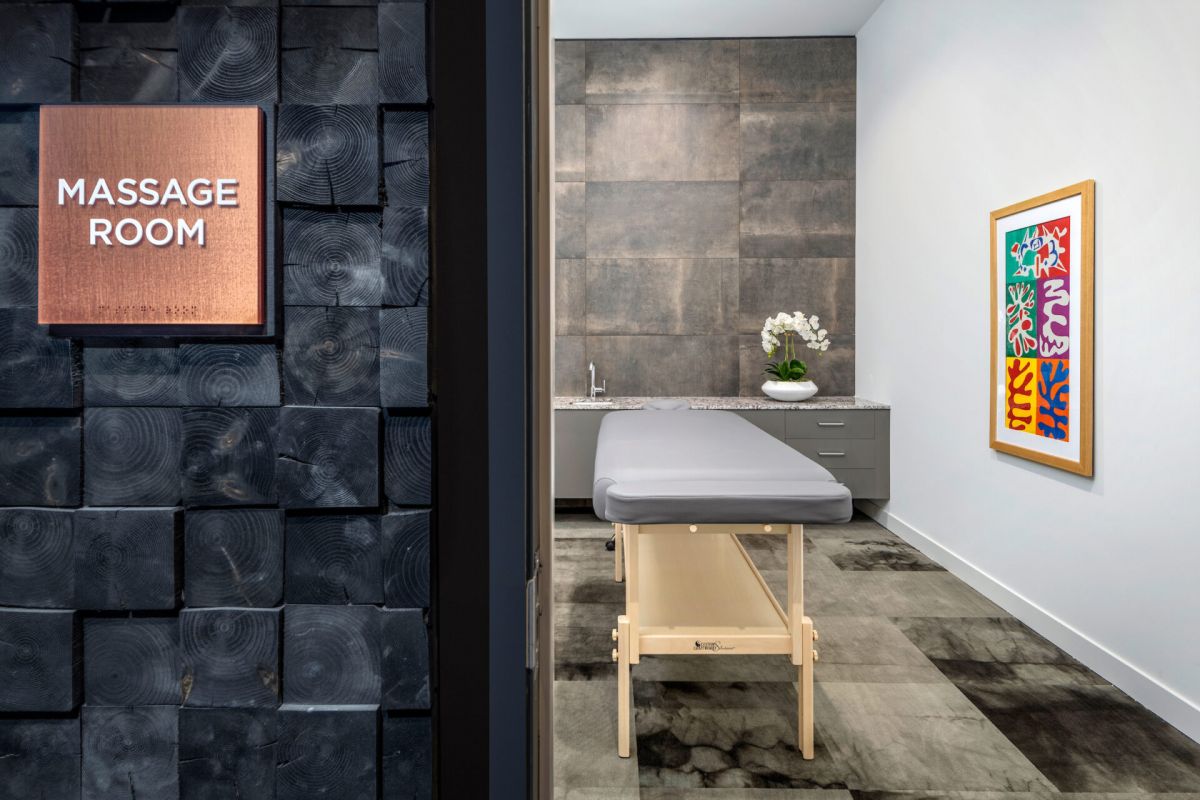 Modern massage room with a massage table, orchid plant, colorful artwork, and a serene atmosphere for massage therapy.