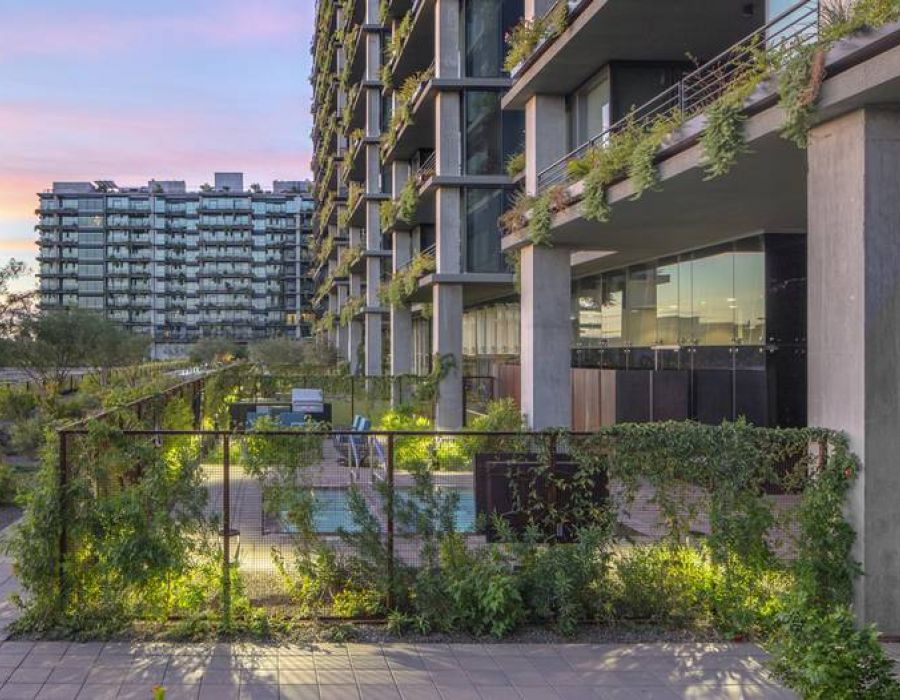 Modern apartment building with plants and greenery growing along fences and balconies at sunset.