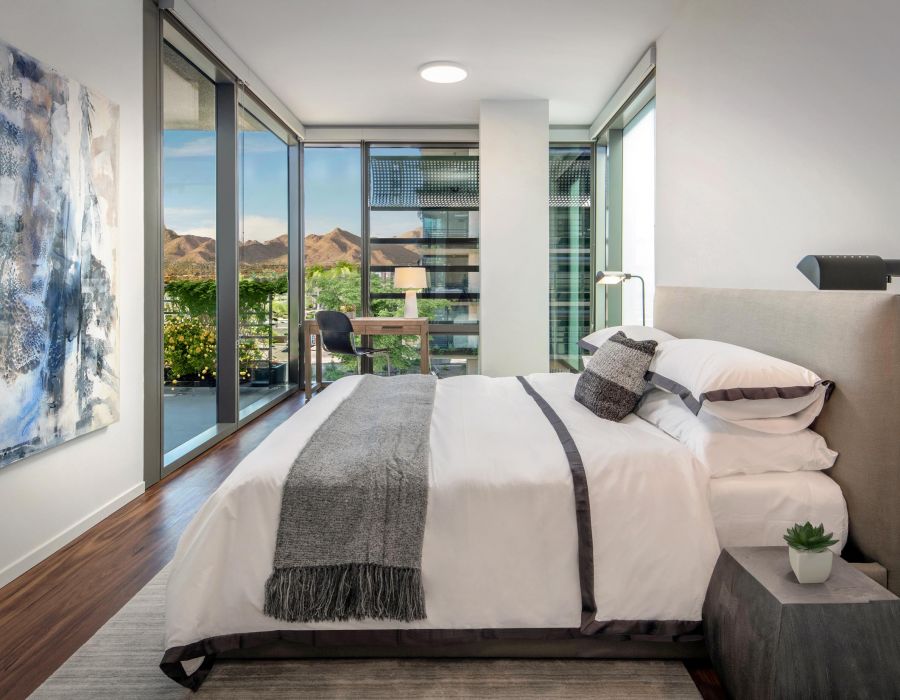 Modern bedroom with large windows, a neatly made bed, and a mountain view in the background.