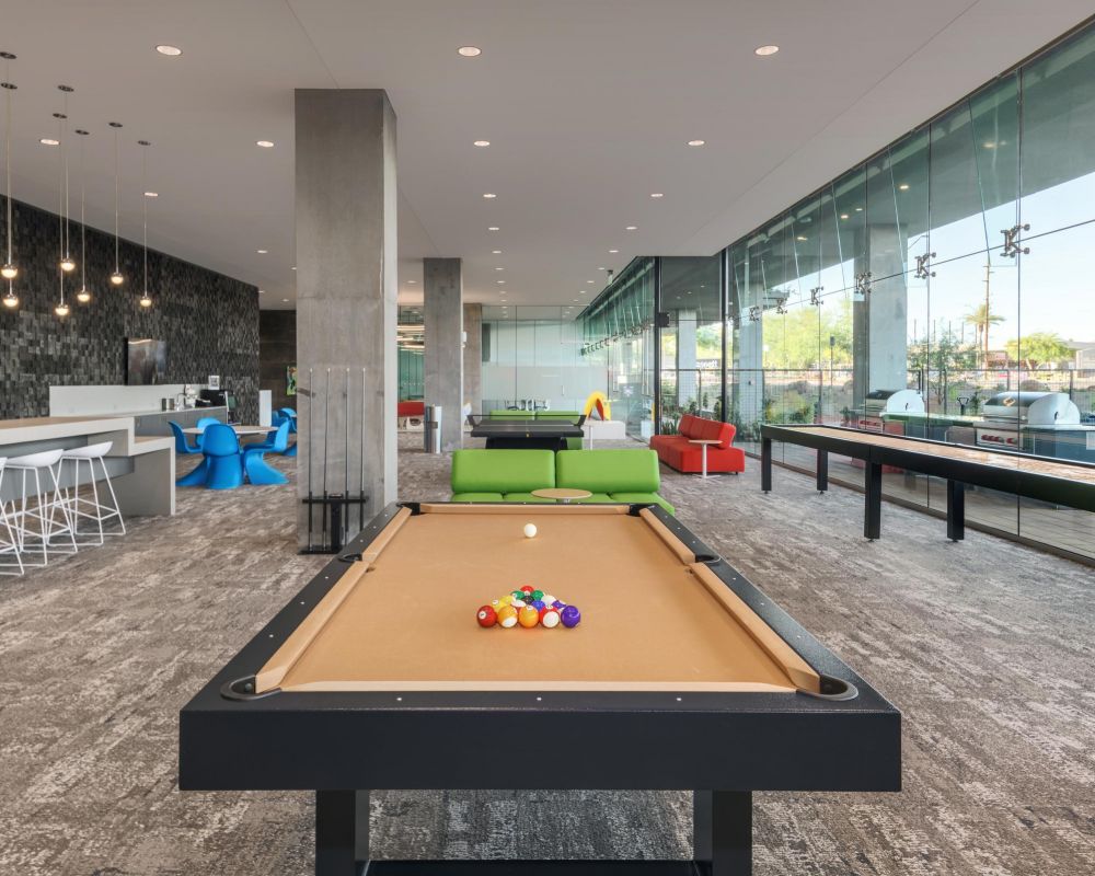 Modern lounge with a pool table, shuffleboard, bar seating, and large floor-to-ceiling windows.