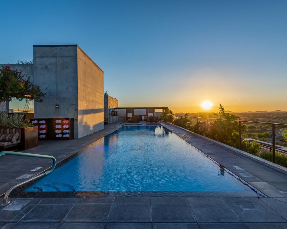 Rooftop swimming pool with a clear sky and sunset view over a city landscape.