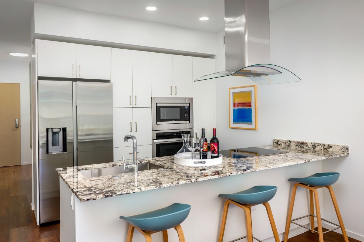 Modern Optima kitchen with white cabinets, granite island, blue stools, and wine bottles on the counter.