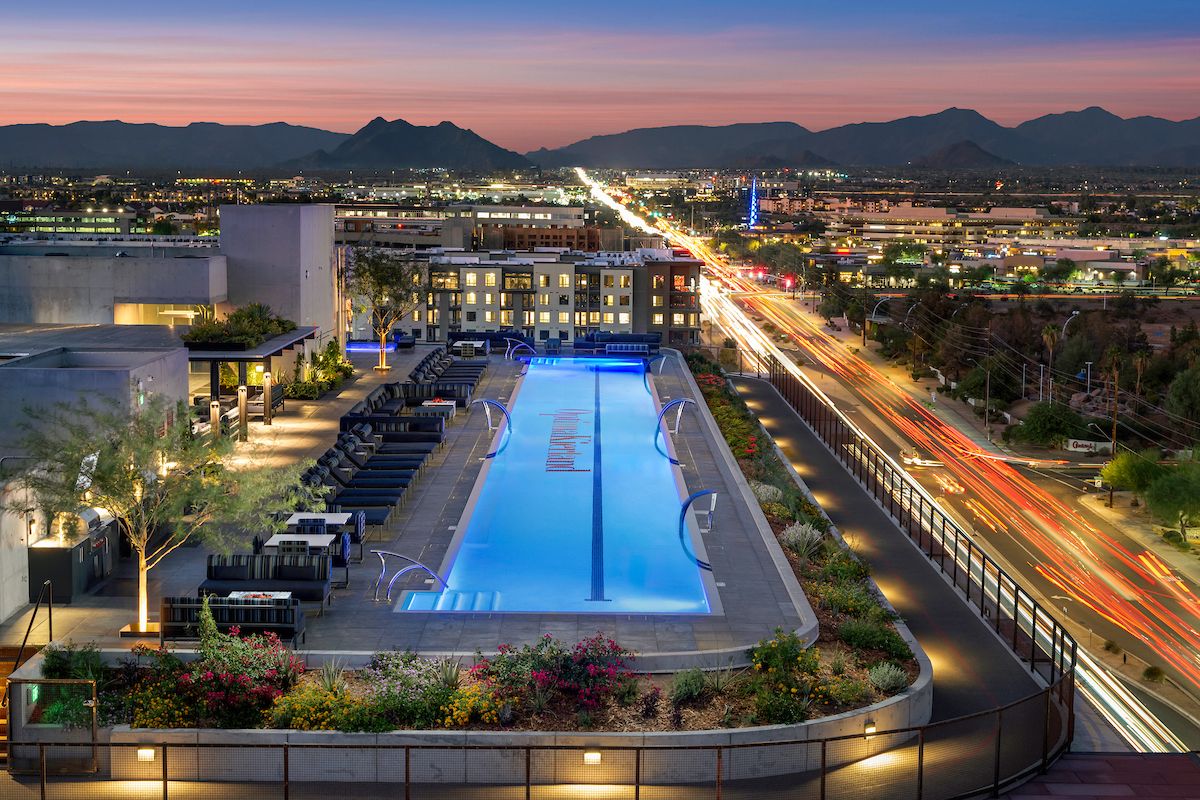 Rooftop pool at 7190-03 Residences lit at dusk, with city lights, lounge chairs, mountains, and Optima Kierland views.