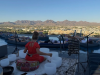 A person in a red dress plays crystal singing bowls for people on pool rafts, a peaceful home preparation scene with mountains in the background.