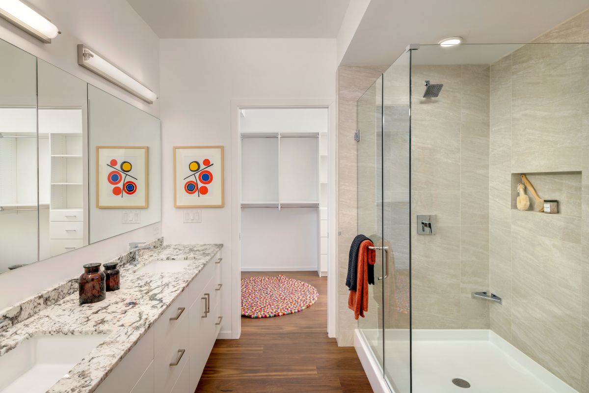 Modern bathroom with double vanity, glass shower, abstract art, and a walk-in closet—showcasing stylish bathroom design throughout.