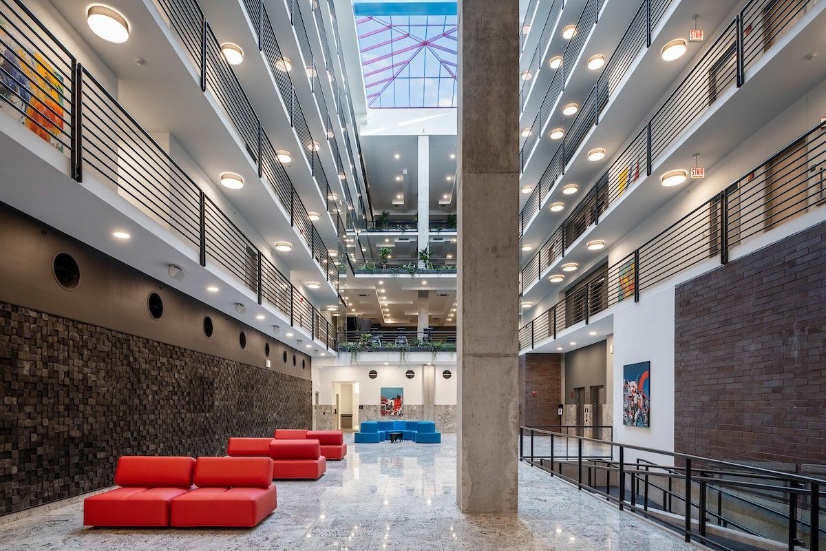Modern atrium with red couches, multiple floors, glass ceiling, and bright lighting that welcomes ample sunlight for radiant health.