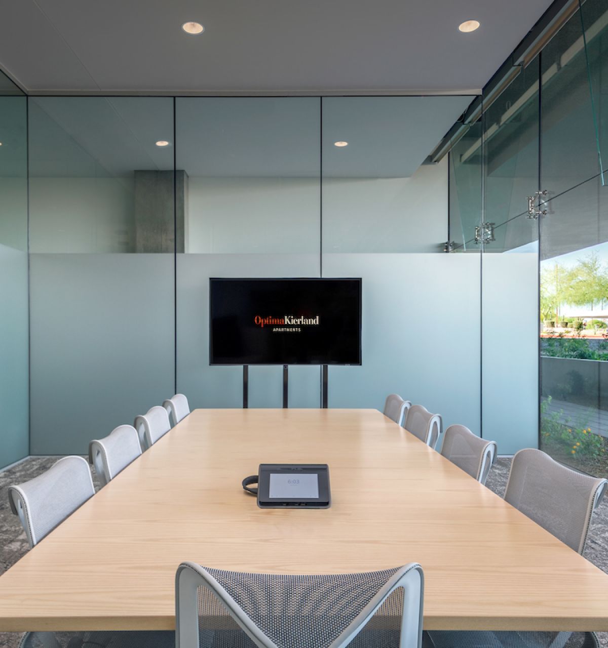 Modern conference room with a long table, chairs, TV screen, glass walls, and an Optima work design for a home office feel.