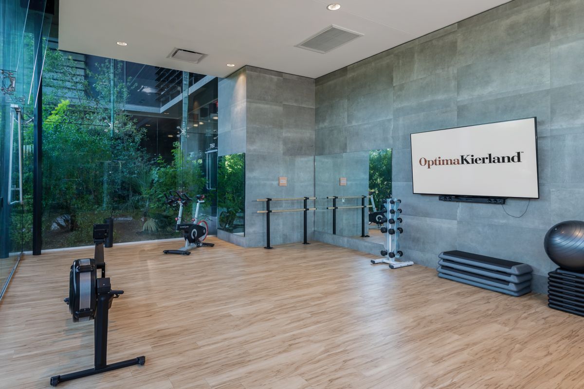 Modern studio gym at Optima Kierland Apartments with exercise bikes, weights, ballet barre, yoga ball, and large windows overlooking greenery.