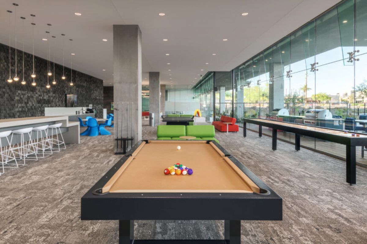 Modern game room with a billiards table, bar seating, lounge chairs, and large windows that foster social connection.