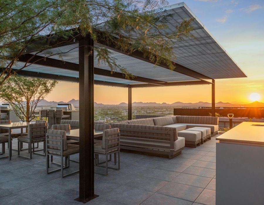 Modern outdoor patio with lounge seating and dining area at sunset, overlooking distant mountains and a cityscape.