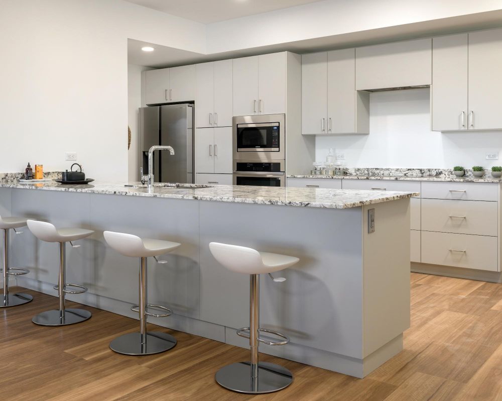 Modern kitchen with white cabinets, granite island, four bar stools, and stainless steel appliances.
