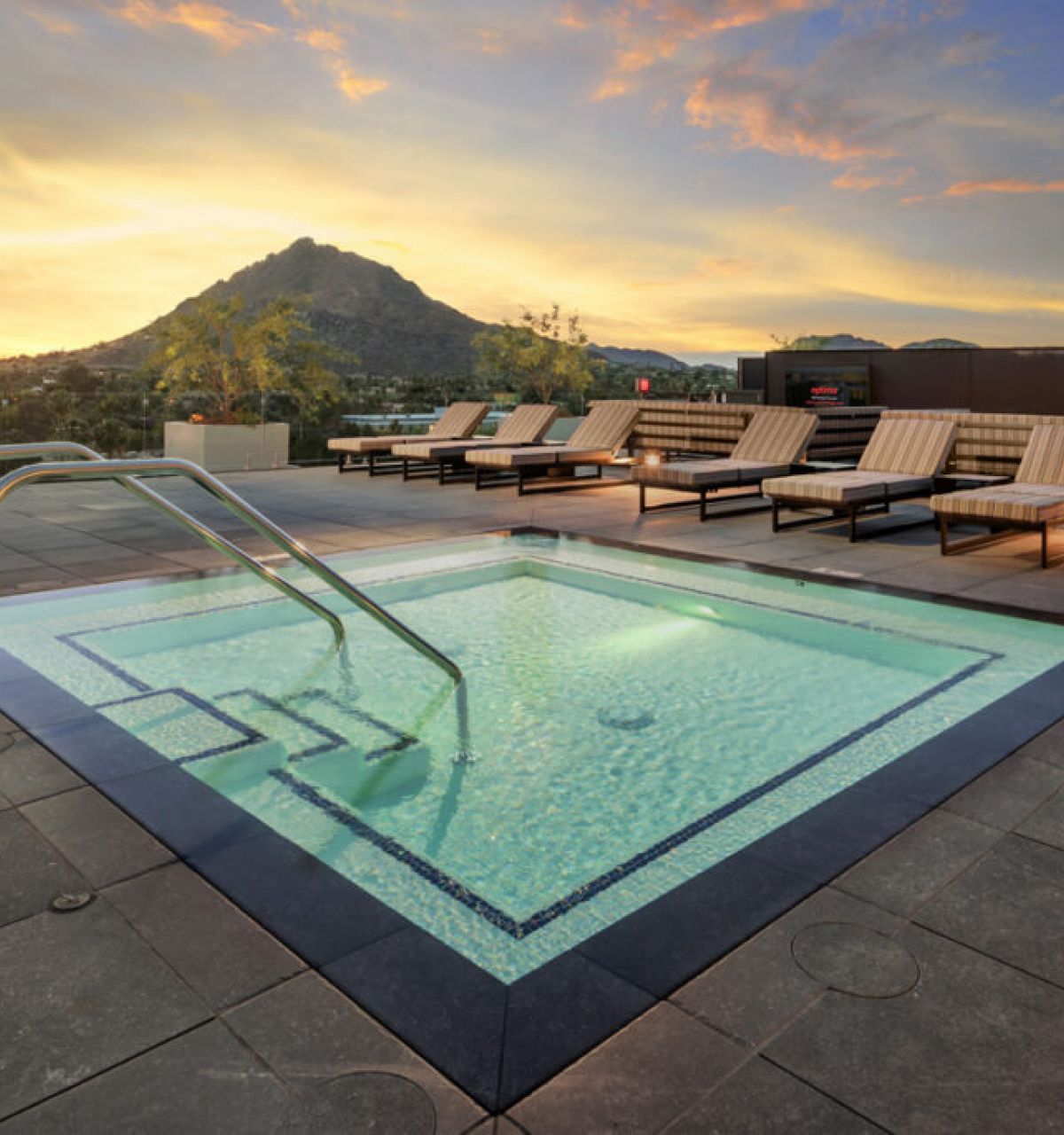 A rooftop hot tub with lounge chairs offers scenic living as it overlooks a mountain at sunset.