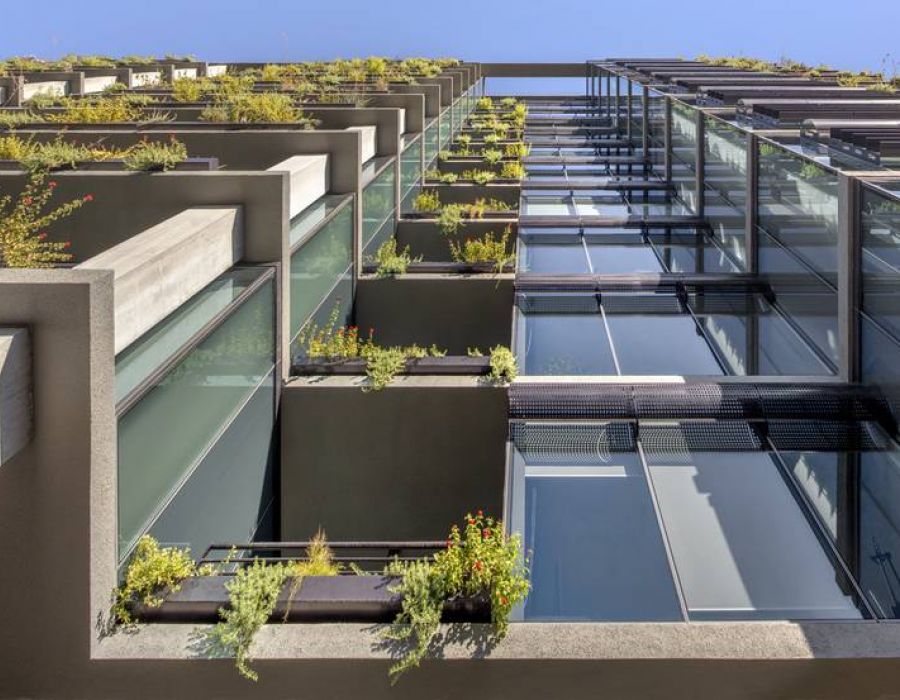 Low-angle view of a modern building with plants growing in planters on each balcony and ledge.