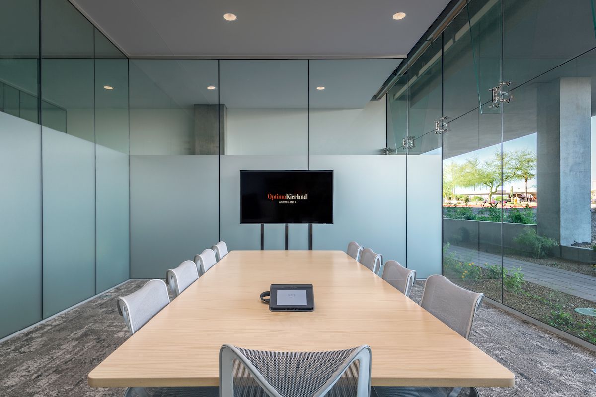 Modern conference room with a long table, chairs, TV screen, glass walls, and an Optima work design for a home office feel.