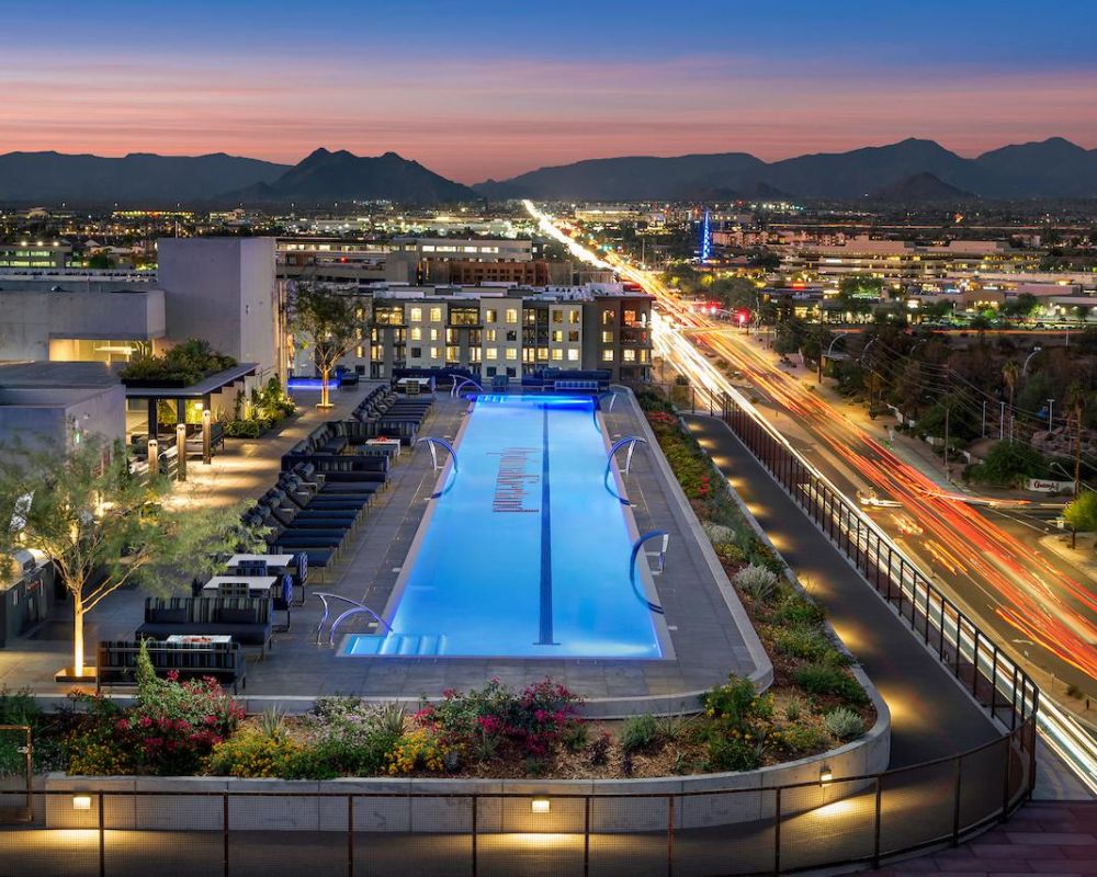 Rooftop pool at dusk overlooking a city with mountains and streaks of car lights in the distance.
