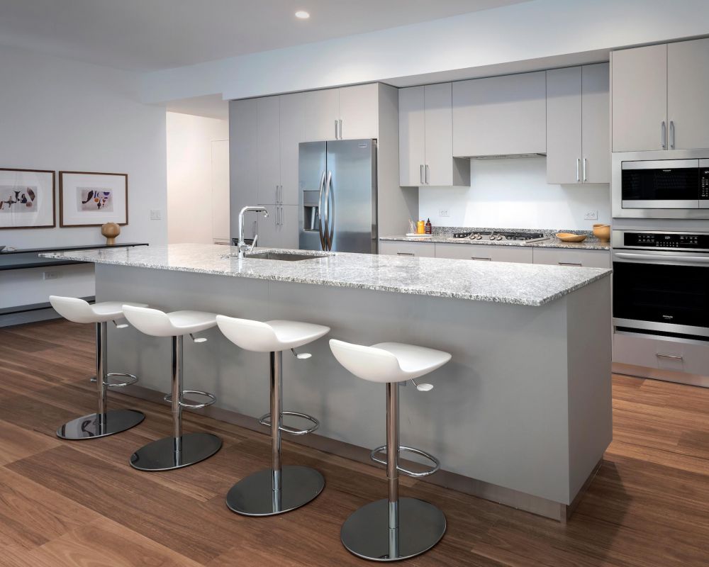 Modern kitchen with gray cabinets, stainless steel appliances, and four white barstools at a marble island.