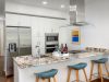 Modern Optima kitchen with white cabinets, granite island, blue stools, and wine bottles on the counter.