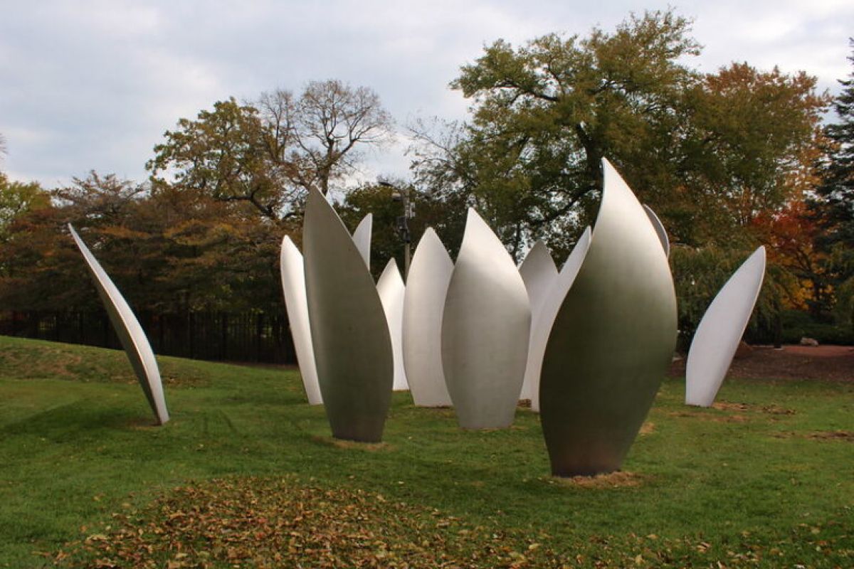 Metal leaf-shaped sculptures stand on grass in Jackson Park’s Garden of the Phoenix, with trees behind and a cloudy Chicago sky above.