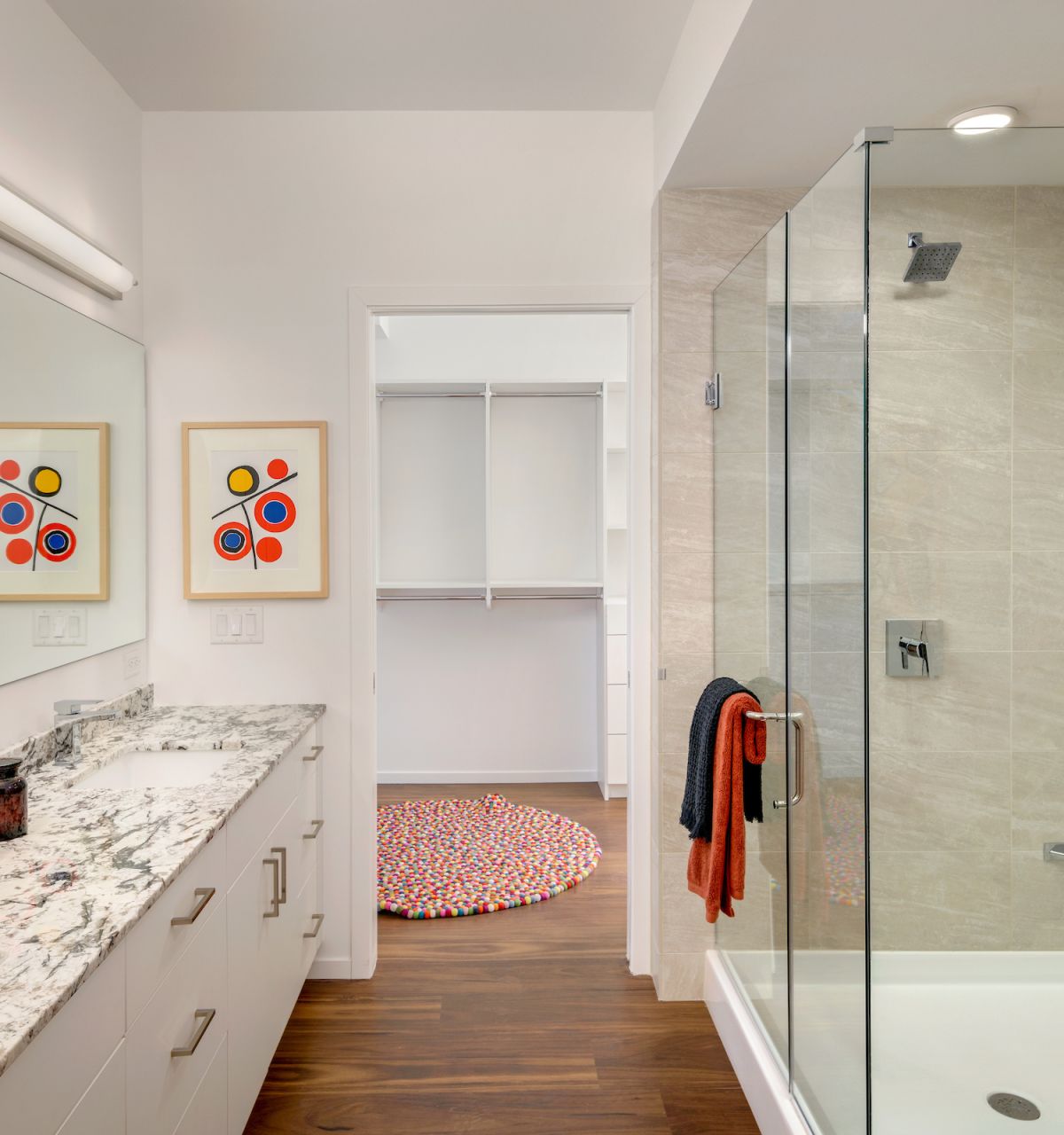 Modern bathroom with double vanity, glass shower, abstract art, and a walk-in closet—showcasing stylish bathroom design throughout.