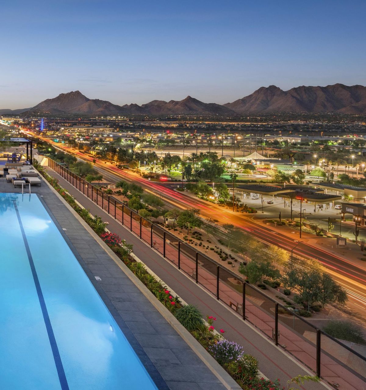 Rooftop pool overlooking a cityscape at dusk with mountains and a busy road in the background.