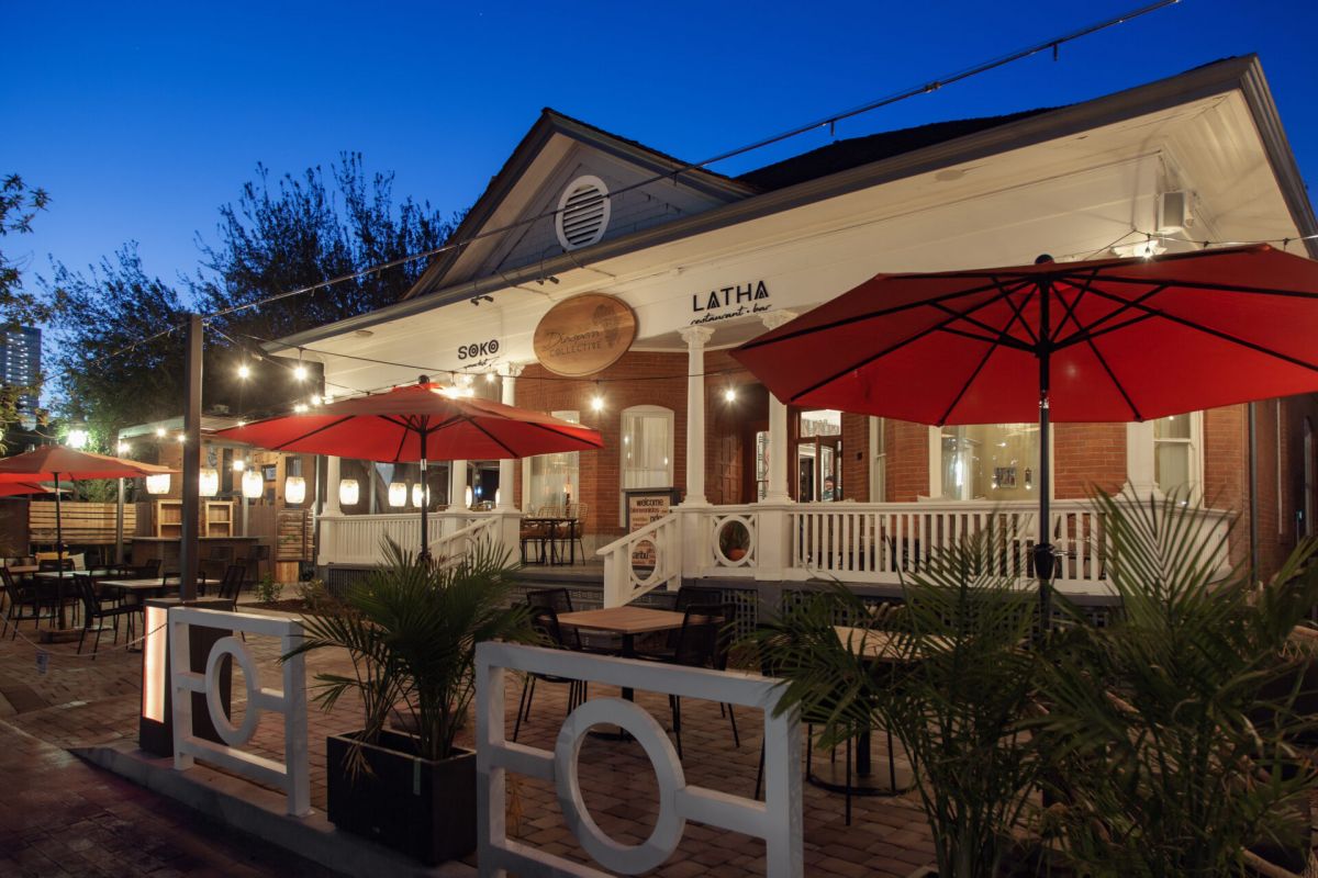 Outdoor dining area at Optima Scottsdale features red umbrellas and string lights at dusk, perfect for discovering history over a meal.