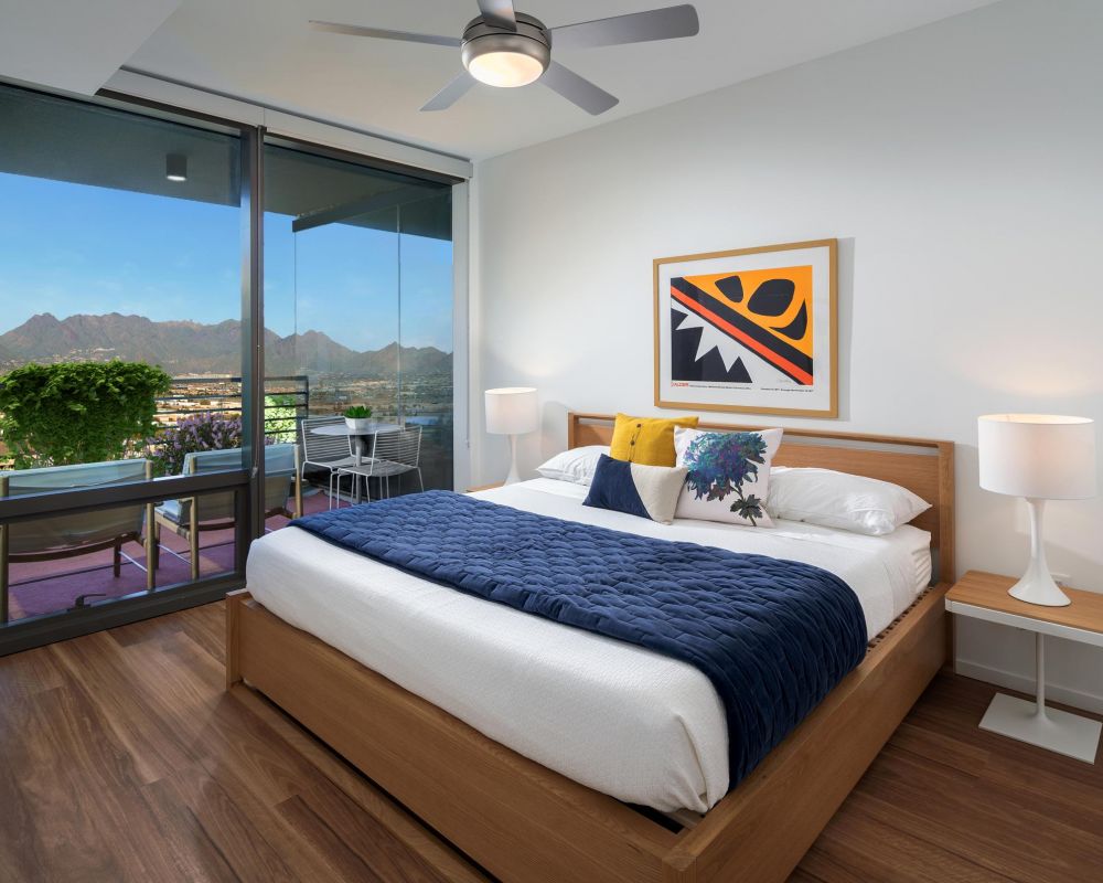 Modern bedroom with a large bed, balcony, mountain view, and colorful artwork above the headboard.