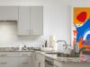 Modern kitchen with gray cabinets, stainless steel appliances, granite counters, and colorful wall art by local artists.