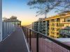 Sunlit walkway with railings between modern apartment buildings, ideal for morning rituals or daily routines amid trees and a distant mountain view.
