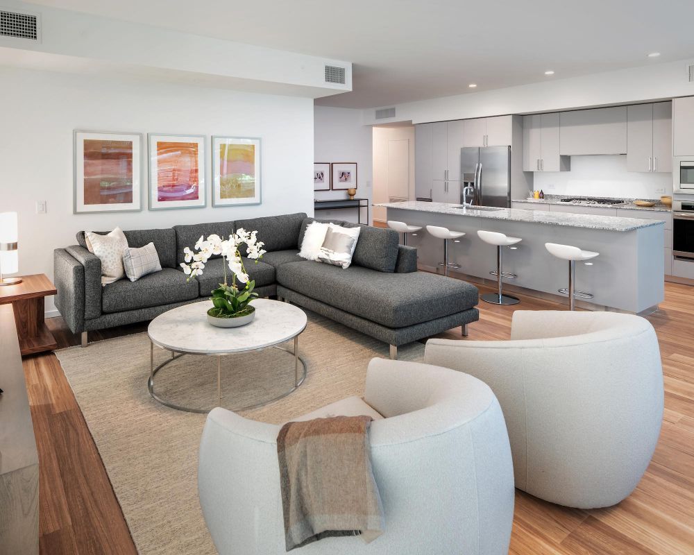 Modern open-concept living room and kitchen with gray sofa, round chairs, and bar stools at a marble island.