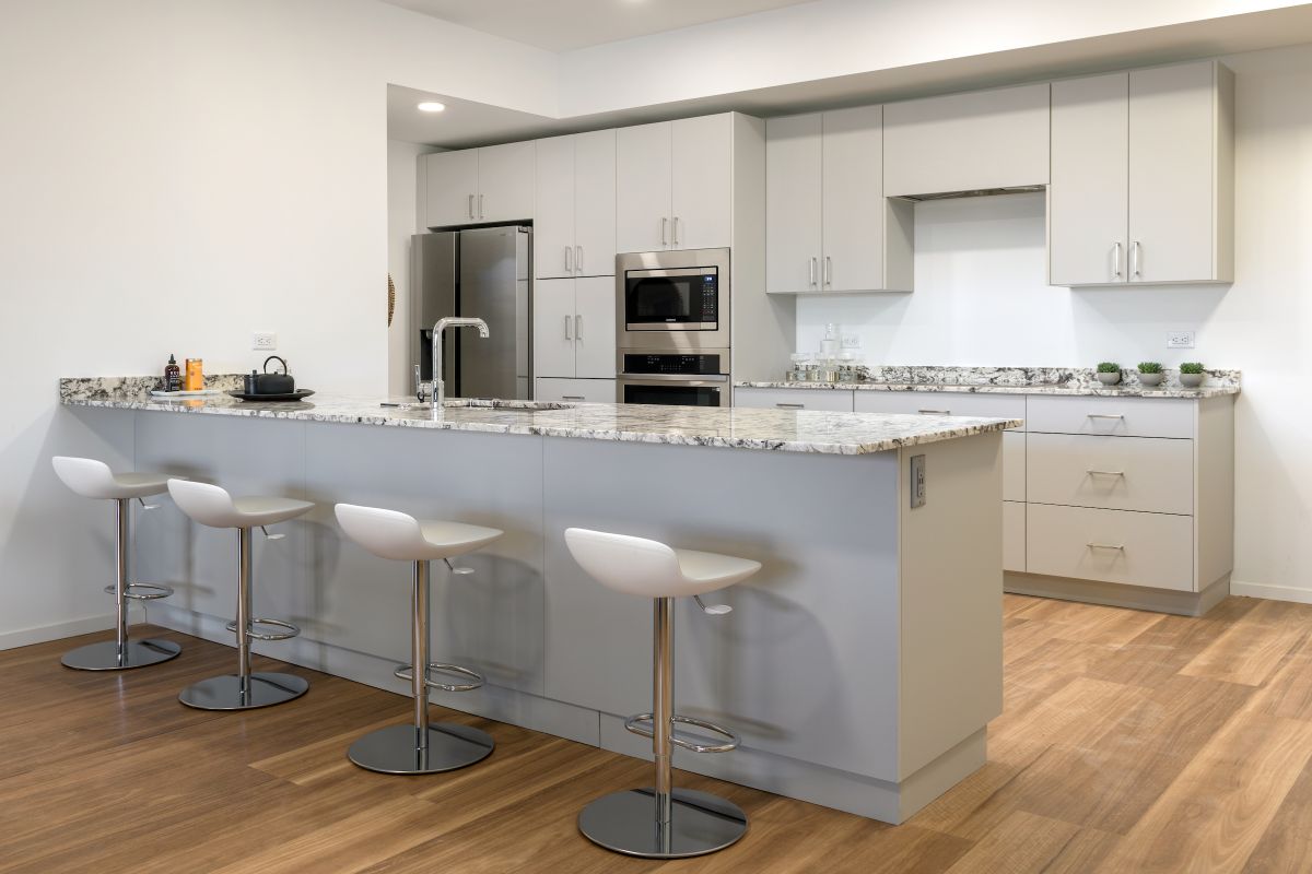 Modern kitchen with white cabinets, granite island, and three white bar stools—perfect for hosting at home on a wooden floor.