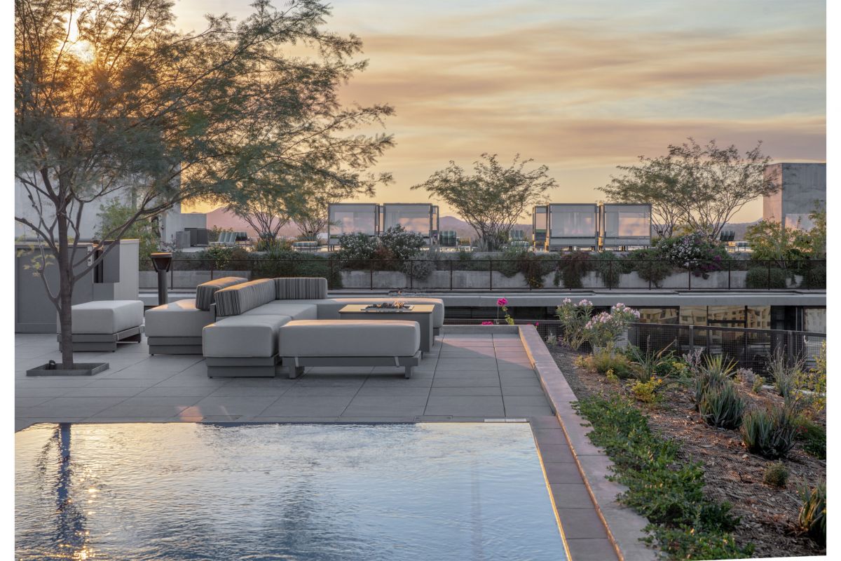 Modern outdoor patio for Optima Residents with sofas, trees, and a reflecting pool at sunset, overlooking the city skyline. Rent now.