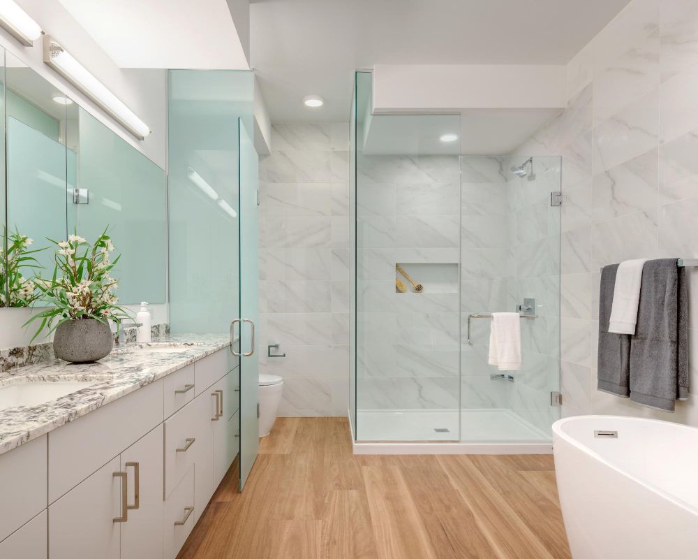 Modern bathroom with marble countertop, glass shower, freestanding tub, and wood flooring.