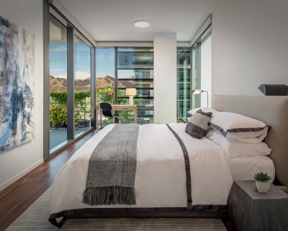 Modern bedroom with large windows, mountain view, a desk by the window, and contemporary decor.