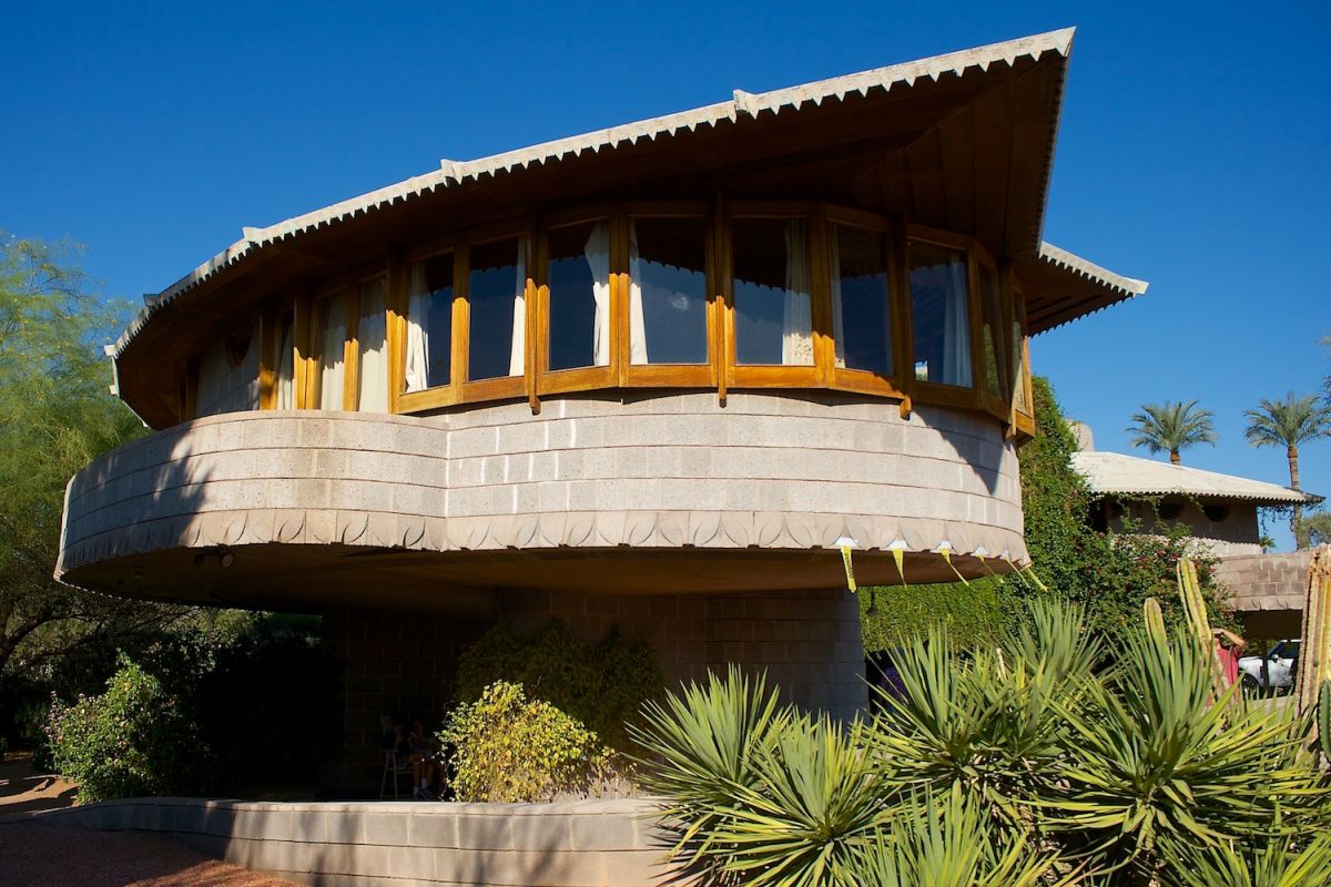 A modern house with curved walls and large windows, echoing Phoenix architecture, surrounded by desert plants under a clear blue sky.