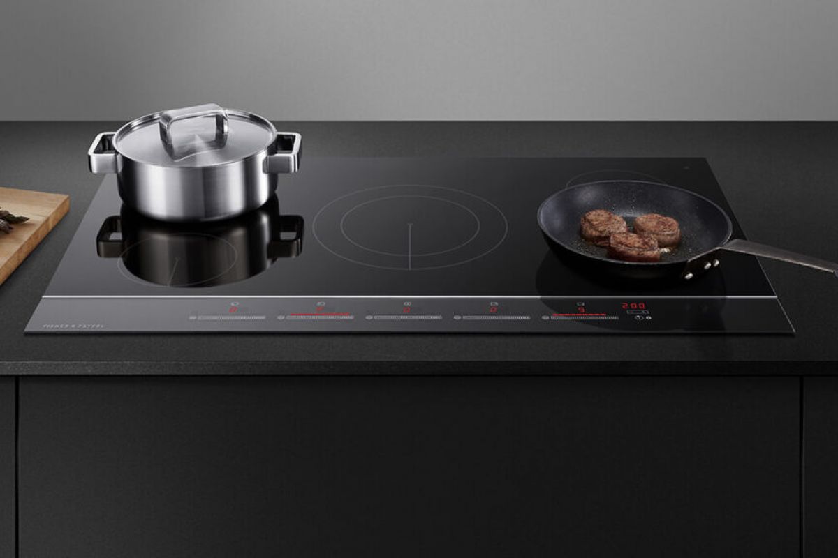 A stovetop with a pot and pan on induction cooktops, cooking food beside a cutting board with asparagus.