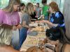 People gather at an Optima Communities table during celebrations, enjoying jewelry, crafts, and henna at a lively community event.