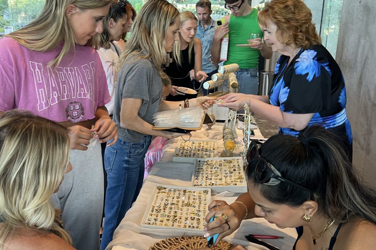 People gather at an Optima Communities table during celebrations, enjoying jewelry, crafts, and henna at a lively community event.