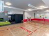 Indoor gym with a basketball court, mini tennis net, green couch, TV, and red accents on the walls and floor.
