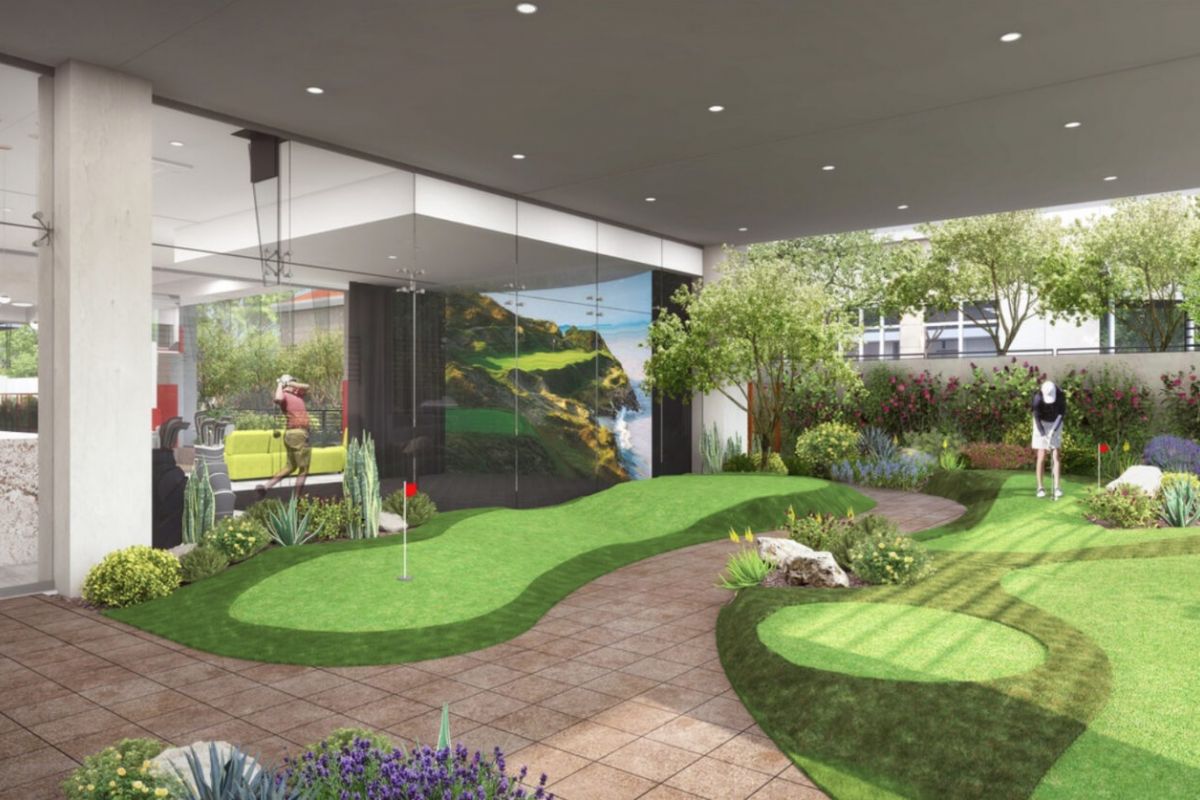 Indoor putting green with artificial grass, plants, and people practicing golf—one of the new amenities at Optima Kierland Apartments.