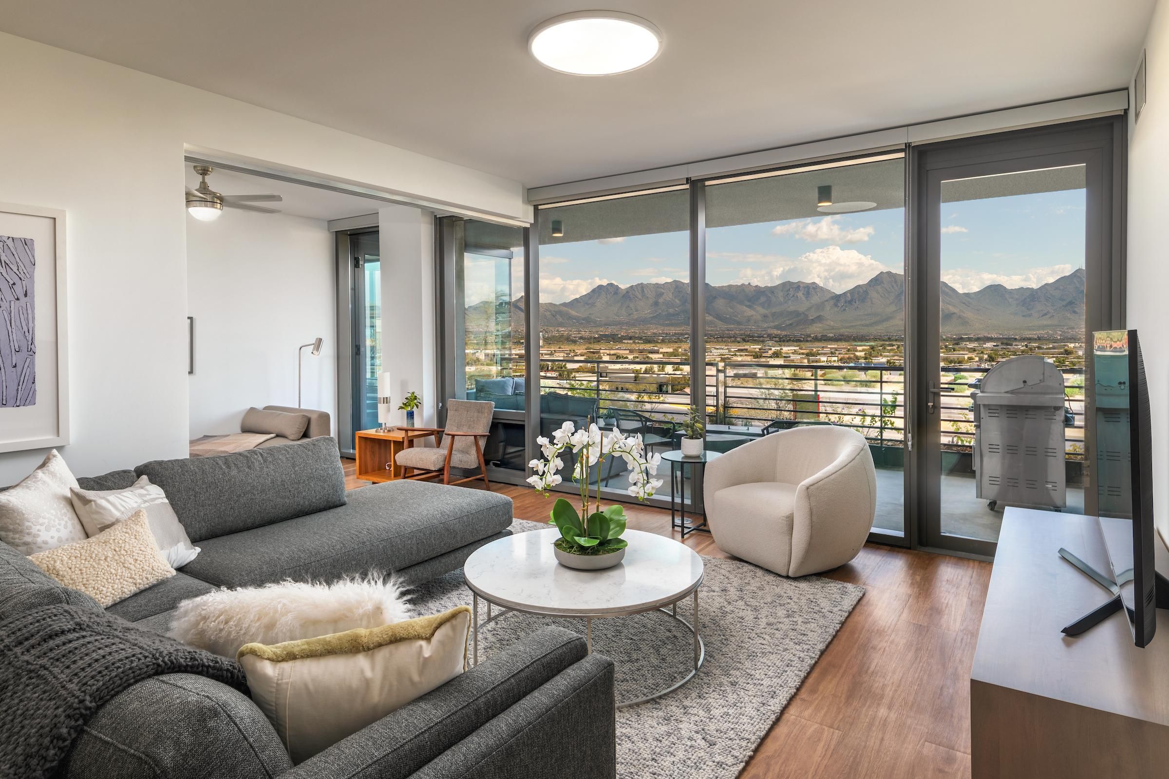 Modern living room with gray sofa, round chair, large windows, and mountain view outside on the balcony.