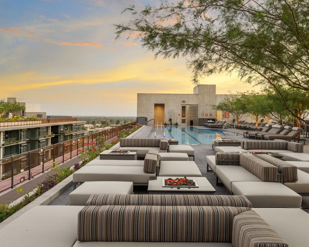 Rooftop pool and lounge area with modern seating at sunset, featuring striped cushions and fire pits.