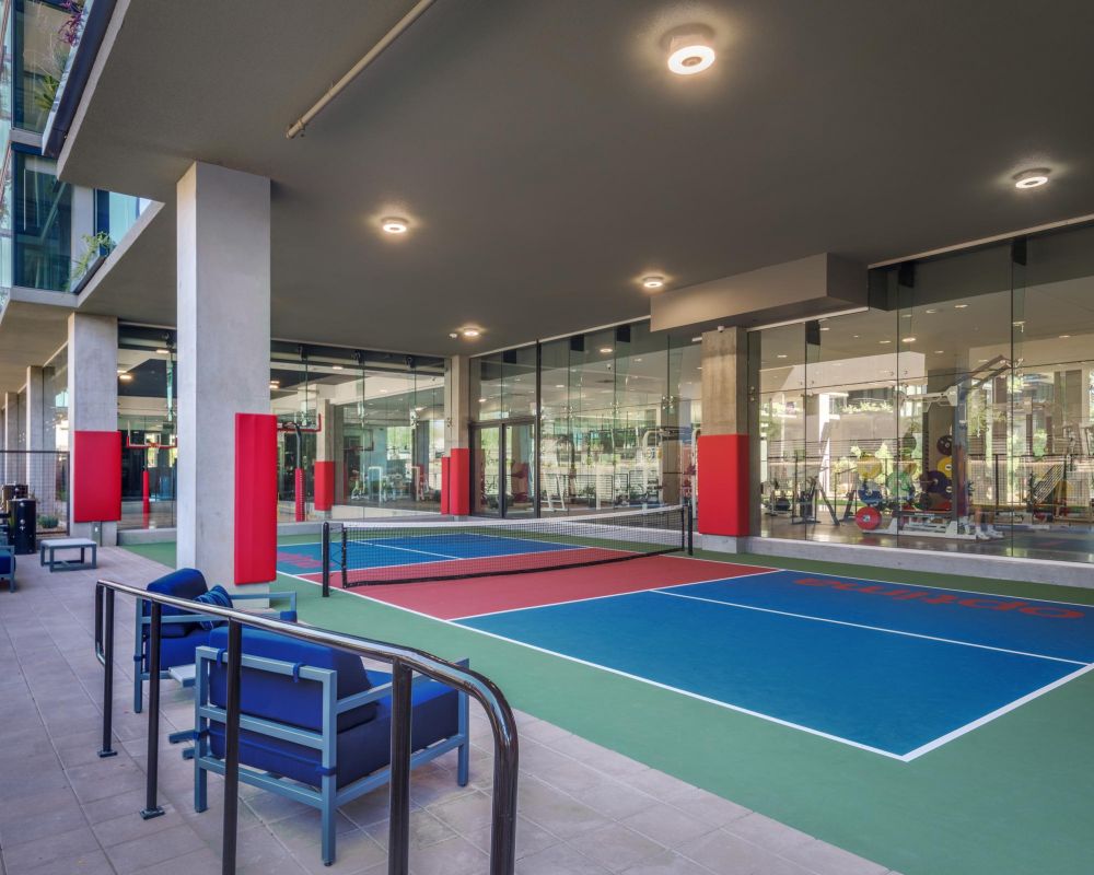 Covered outdoor pickleball courts with seating, adjacent to a glass-walled fitness center.