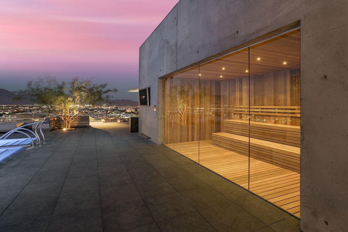A rooftop sauna at Optima Kierland Apartments overlooks a sunset city, with lounge chairs and potted trees completing the Recovery Circuit.