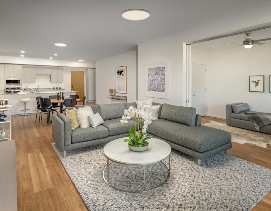 Modern living room with gray sectional sofa, round coffee table, and open kitchen in the background.